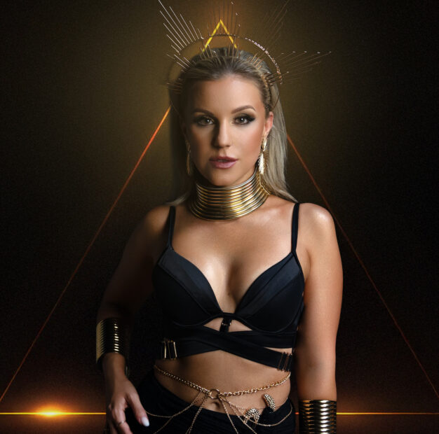 Natalie Holzner in einem schwarzen Outfit mit goldfarbenem Halsschmuck vor dunklem Hintergrund