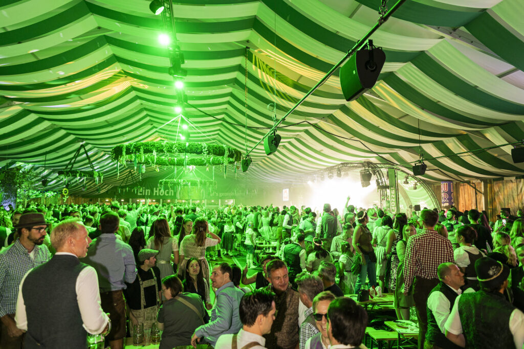 Besucher feiern bei grüner Beleuchtung im Festzelt der Wiener Kaiser Wiesn.