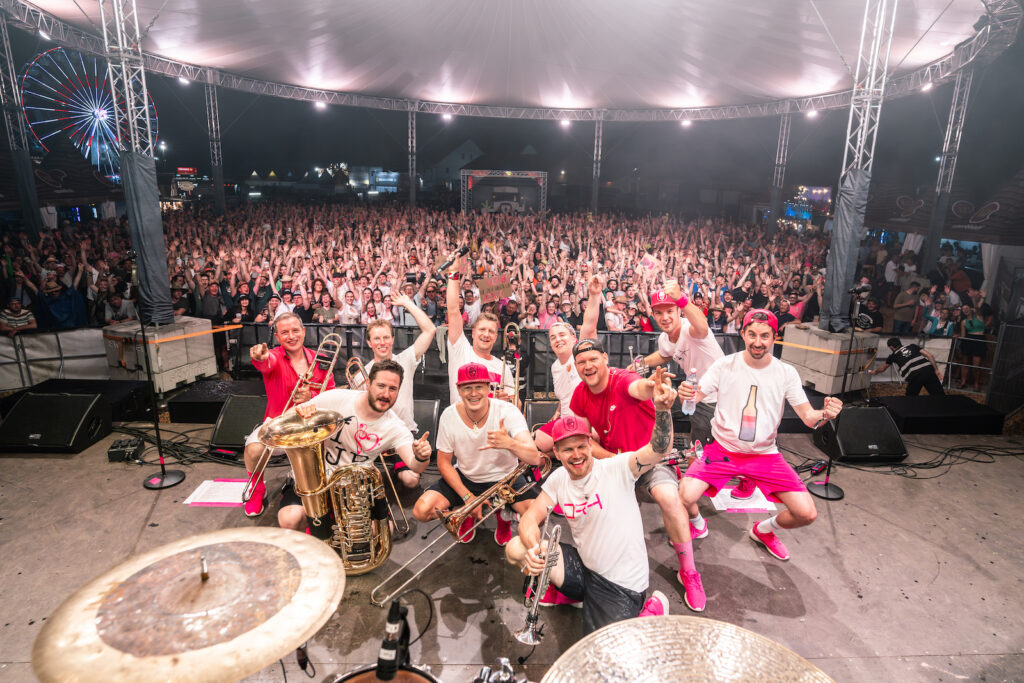Die Band posiert auf der Bühne vor einer jubelnden Menschenmenge in einem Festzelt