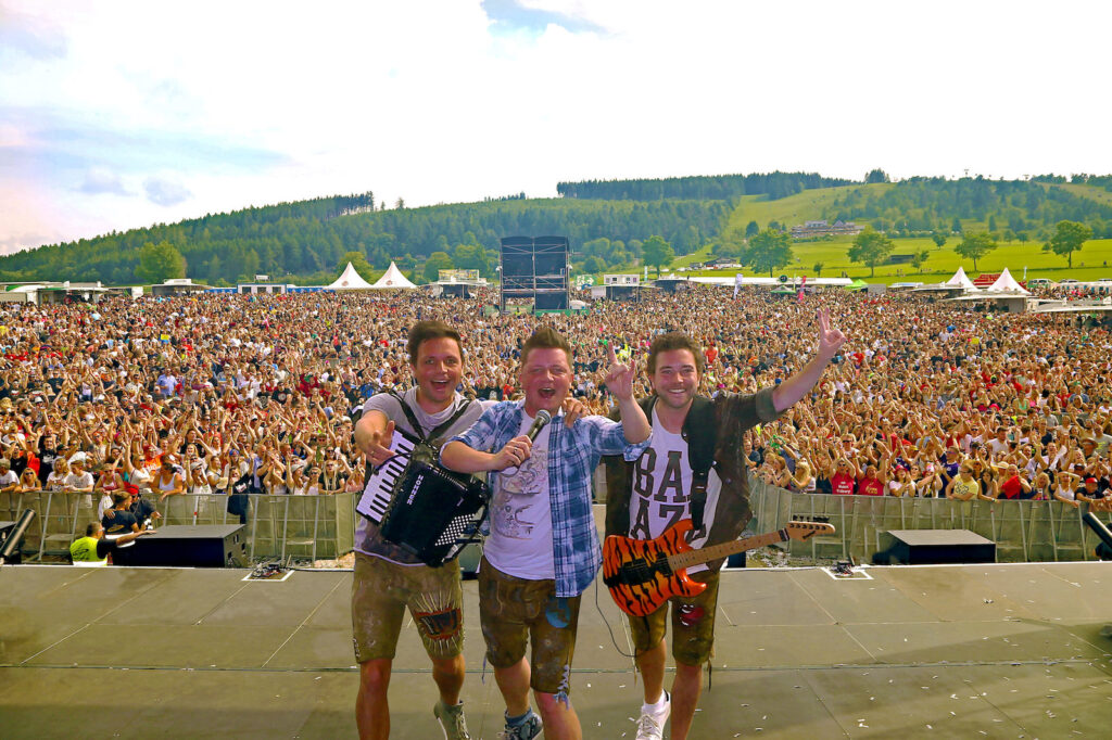 Die Dorfrocker stehen auf einer Festivalbühne vor einer riesigen jubelnden Menschenmenge