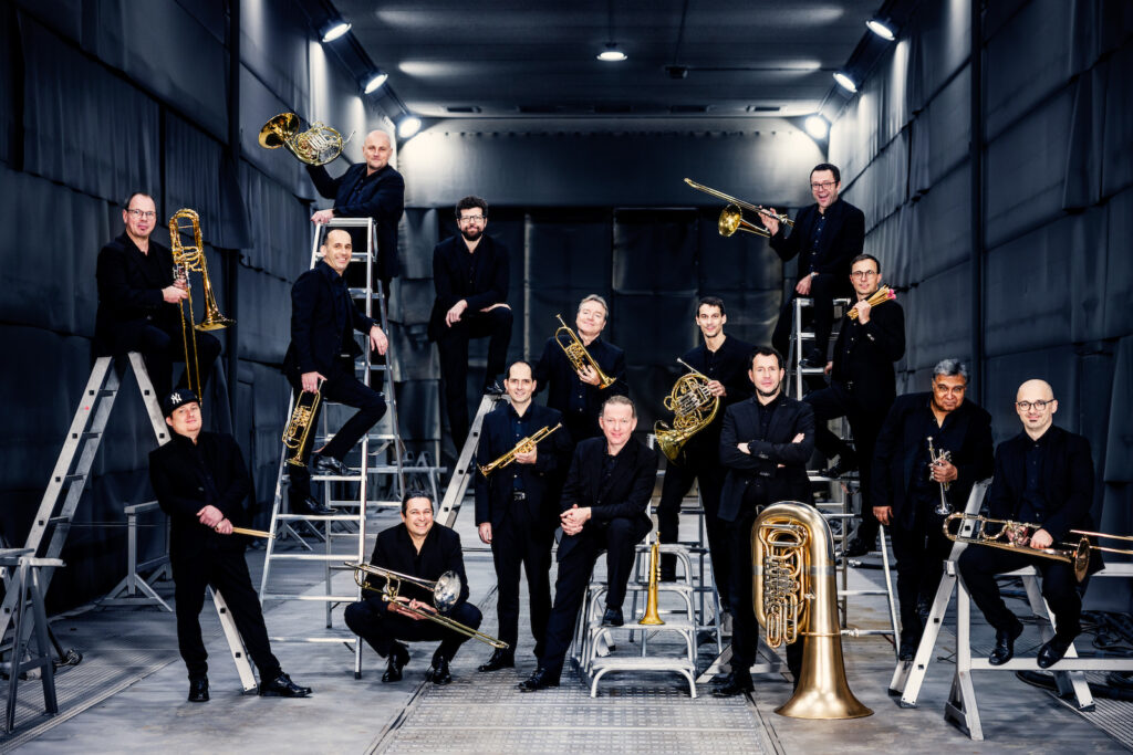 Blechbläserensemble in Schwarz auf Leitern in einer Halle
