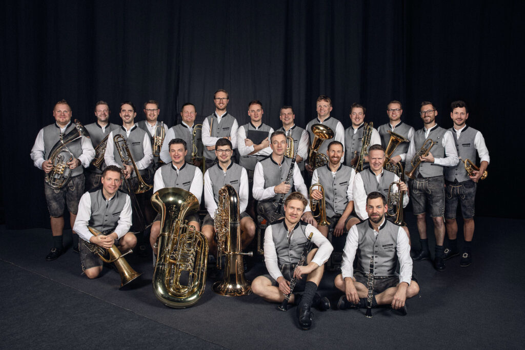 Blasmusikensemble in Trachtenwesten vor schwarzem Vorhang