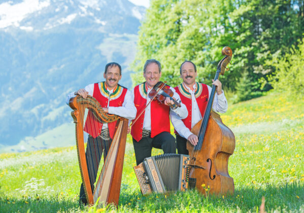 Zellberg Buam mit Harfe, Geige und Kontrabass in traditioneller Tracht vor einer alpinen Bergkulisse
