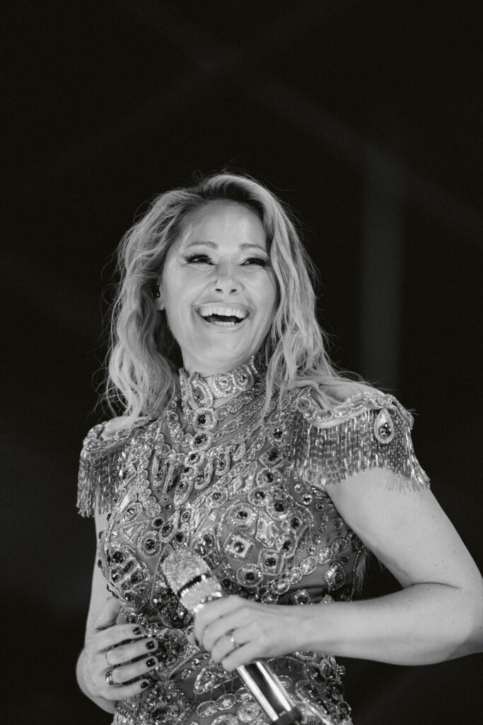 Helene Fischer lacht auf der Bühne in einem mit Perlen und Steinen besetzten Kleid, sie hält ein Mikrofon in der Hand, Schwarz-Weiß-Aufnahme im Hochformat
